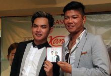 Dua pria berpose dalam sebuah acara musik sambil memegang sampul album