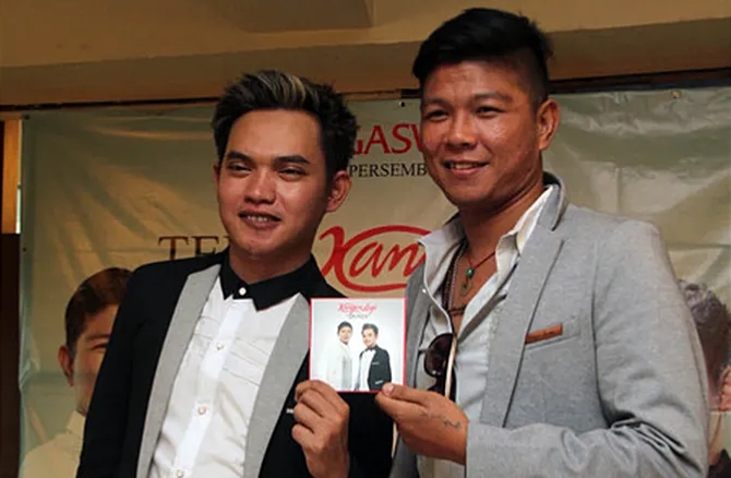 Dua pria berpose dalam sebuah acara musik sambil memegang sampul album